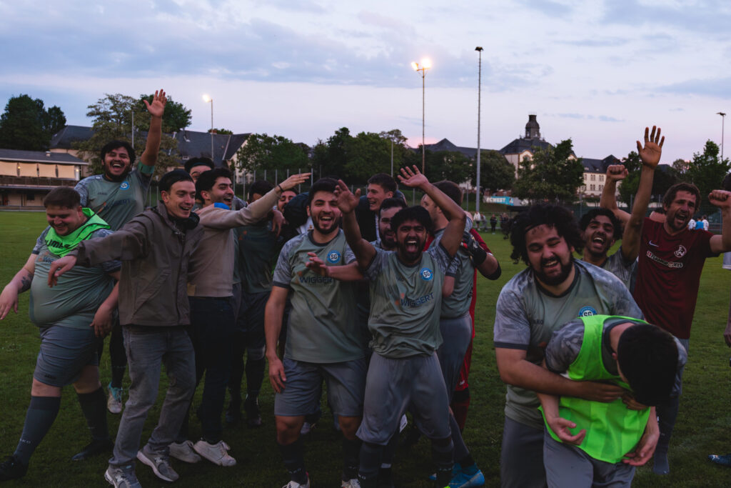 Spieler der SpG Nordweststadt 2 stehen lachend mit erhobenen Armen zusammen auf dem Platz.